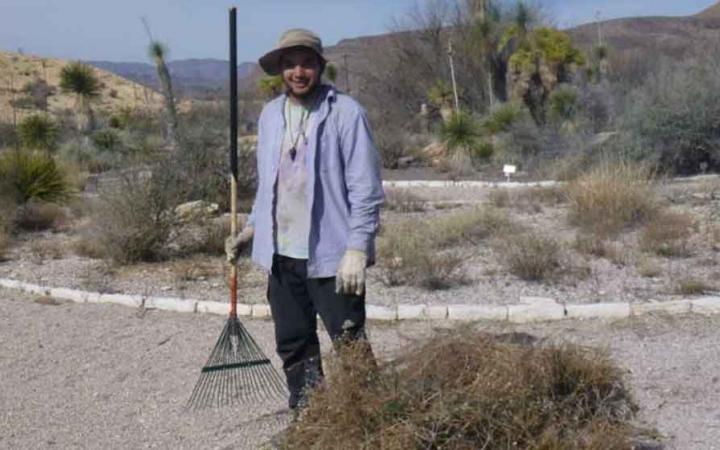 a student holds a rake and stands beside a pile of brush while participating in a service project with outward bound